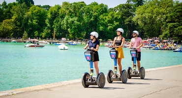 Une guide et ses deux clients à Segway qui se déplacent au bord du lac d'Annecy sous le soleil.